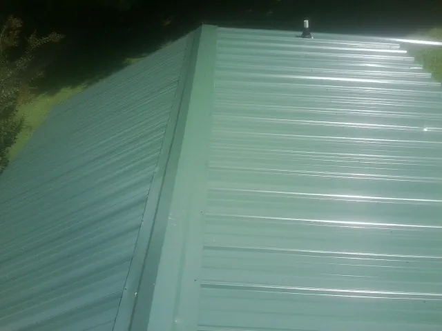 New green metal panels meeting at the ridge of a roof — Flat Roof Repair work by our crew in Freeman